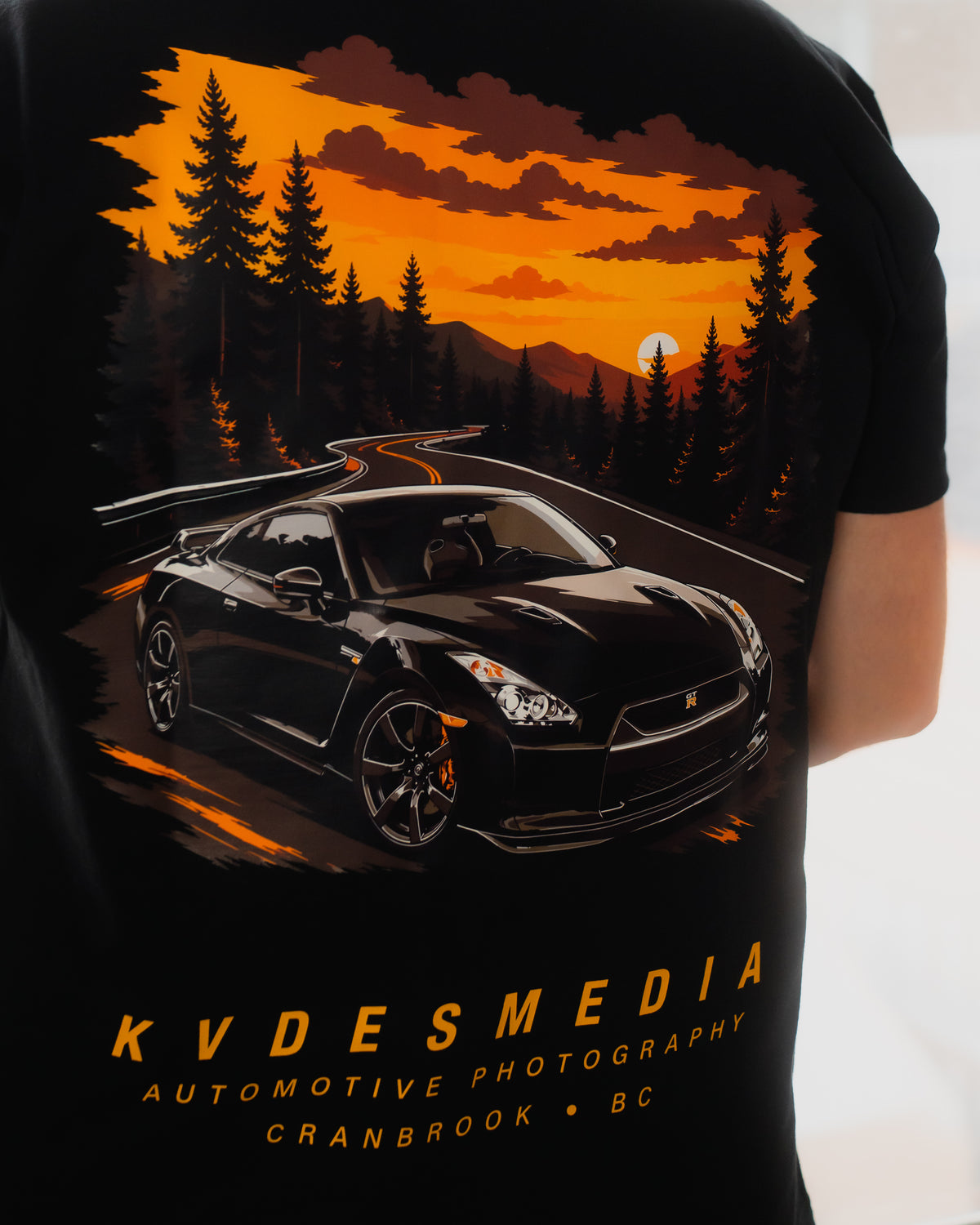 Back graphic of KVDESMEDIA x Aspect T-Shirt featuring a black Nissan GT-R driving on a mountain road at sunset