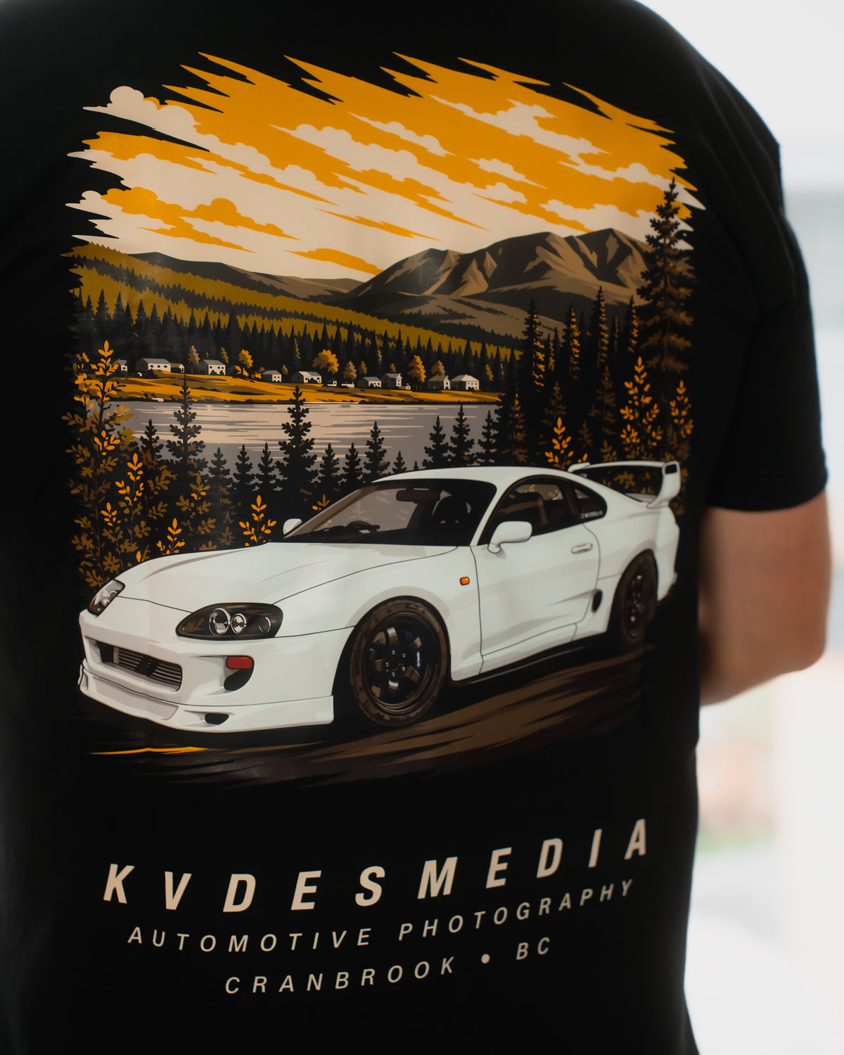 Back graphic of KVDESMEDIA x Aspect T-Shirt featuring a white Toyota Supra with a mountain and lakeside landscape